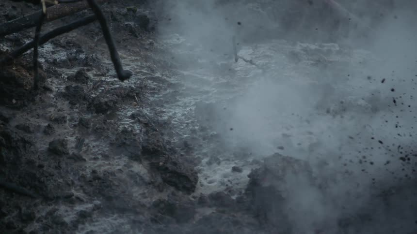 Mud slides down a short slope in a moving stream of water as a mist forms around it