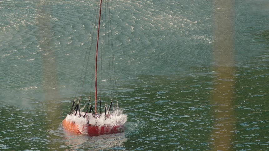 Large orange bucket suspended on a cable from a firefighting helicopter collecting water on a lake