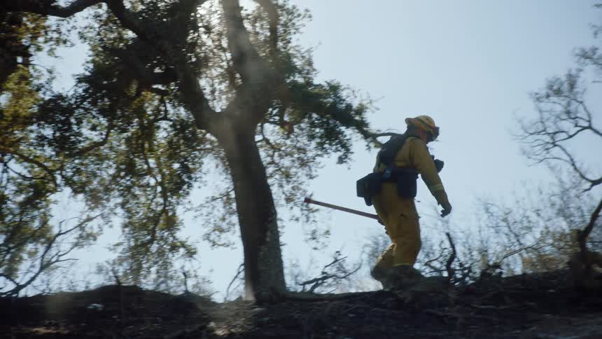 Firefighters climb slope then one leaves and the other moves to dig at ground