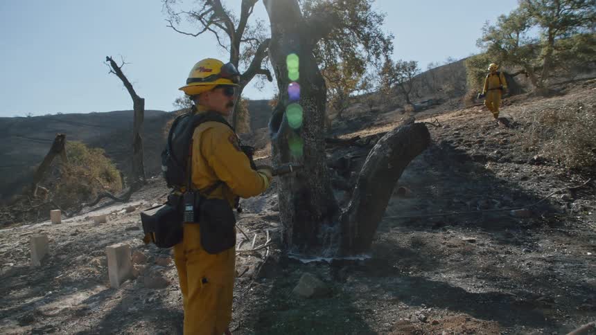 A firefighter walks down a hill towards another firefighter who is pulling on a hose