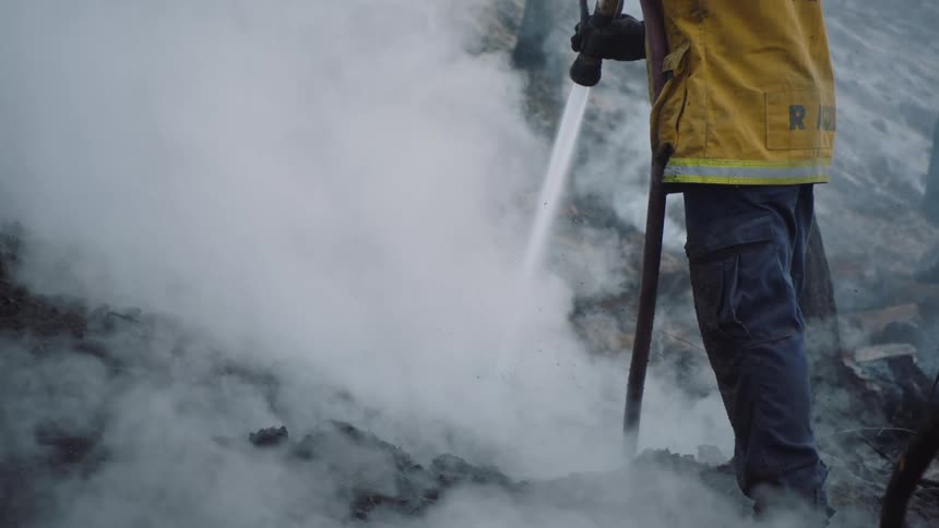 A firefighter using a hose to spray the ground creating steam and mist to form on the surface