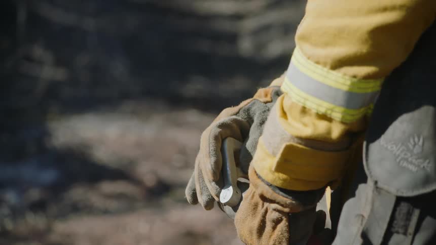 Firefighter standing outdoors sprays water from firehose briefly