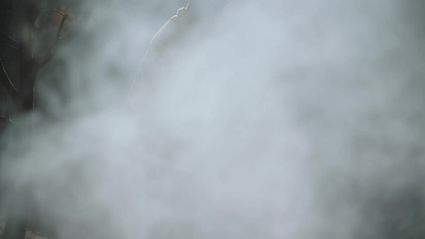 A fireman standing around smokey grounds as he turns and starts to walk away