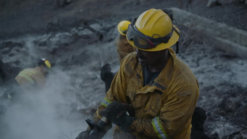 Firefighters finish putting out fire on charred ground within concrete enclosed area