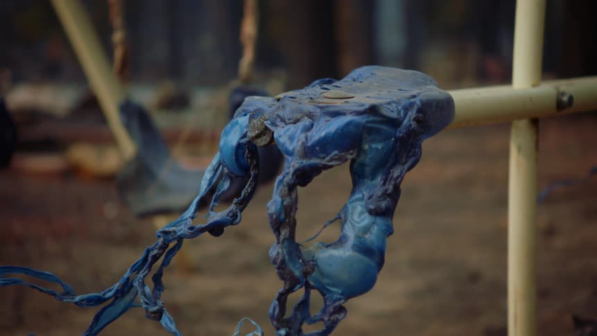 Melted blue plastic on a yellow bar next to a swing set