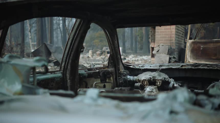 Interior view of a burned out car and the aftermath of a fire recently extinguished in the background
