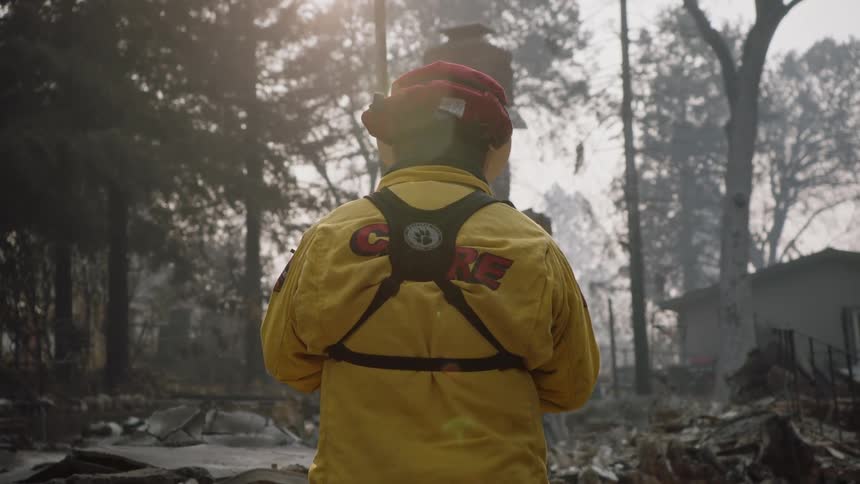 Firefighter examines debris remaining from home near conifer forest