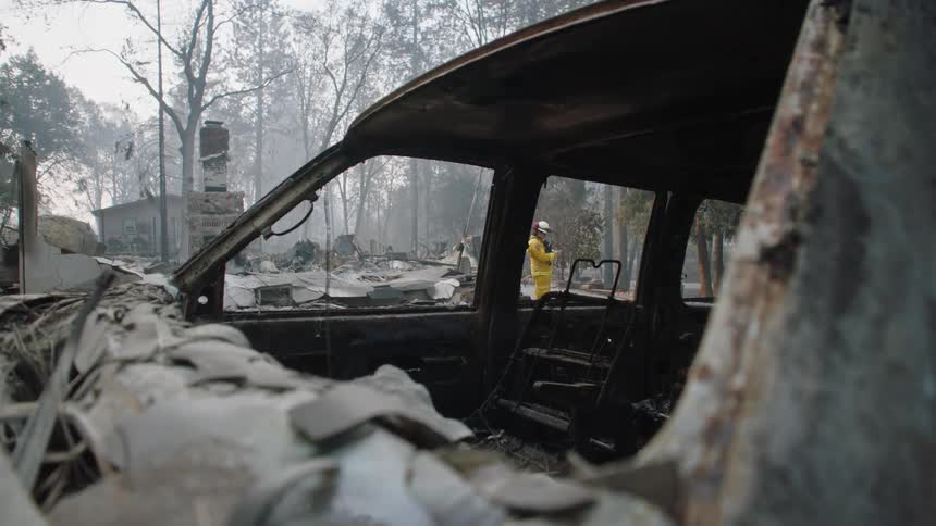 A burnt vehicle and a fireman standing near burnt debris and rubble