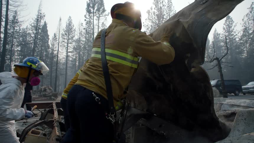 Firefighters wearing yellow protective gear moving the burnt remains of a burned down structure