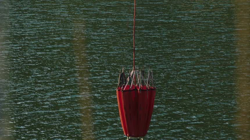 A bucket is lowered into the lake on a cable and it splashes as it hits the water