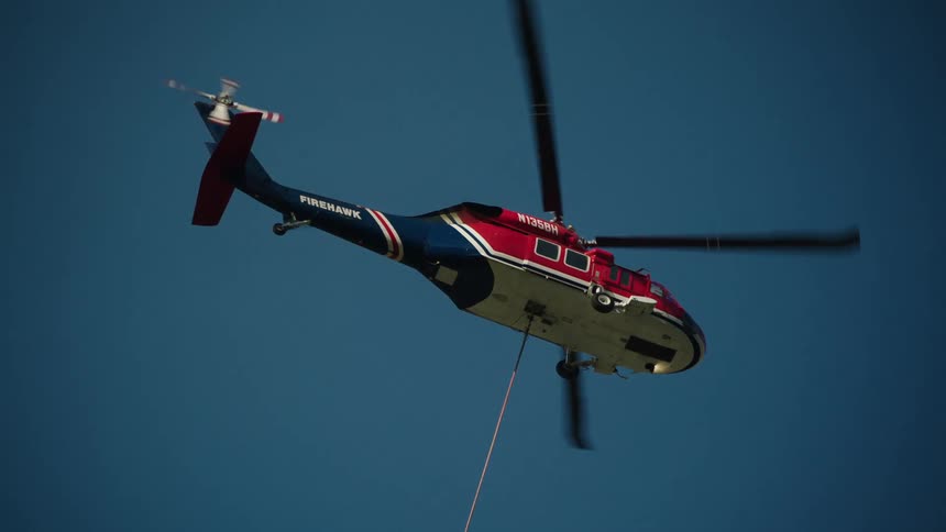 A helicopter flies through the air pulling a tight cable under it