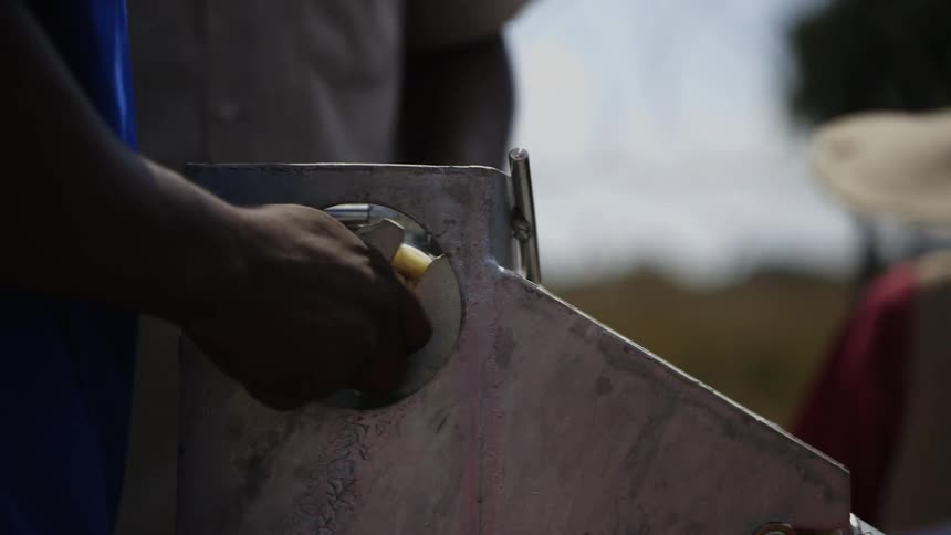 One of several men standing around machine tightens nut by hand
