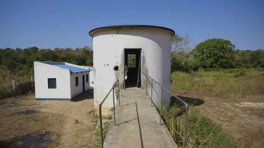 In cluster of buildings a walkway leads to door of circular building with a holed wall