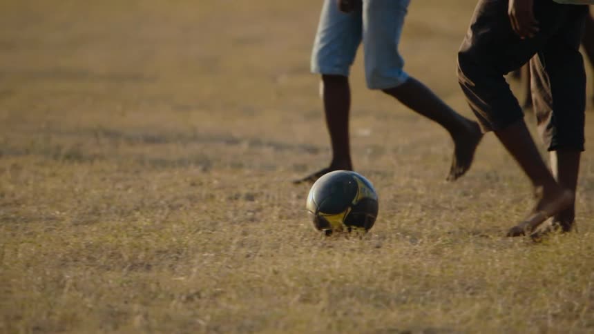 Youths walk slowly then start running while playing soccer barefoot