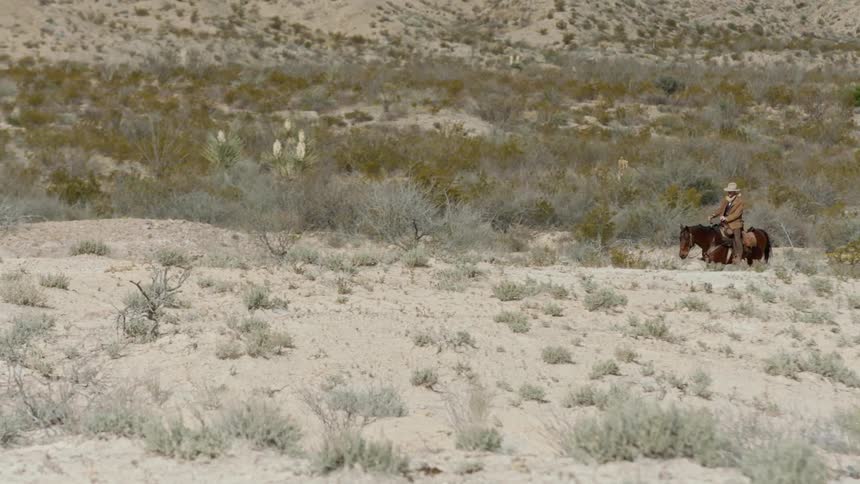 Cowboy rides horse over arid scrubland