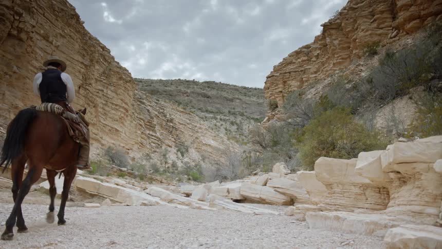 A cowboy rides his horse into a desert canyon and dismounts