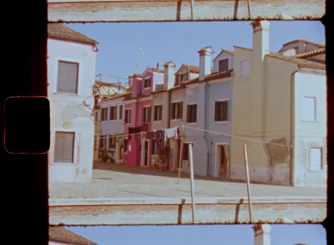 Colorful buildings or rowhouses at the edge or pier of a canal in an Italian city village or town with a road or walkway between the buildings in bright sunshine with blue sky