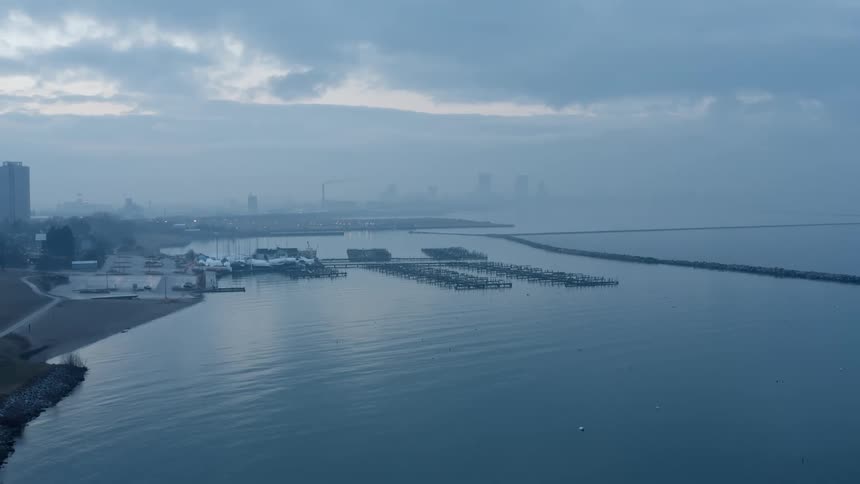 Empty boat docks stretch out from the coast to near the break wall as the metropolitan skyline is barely visible through the fog