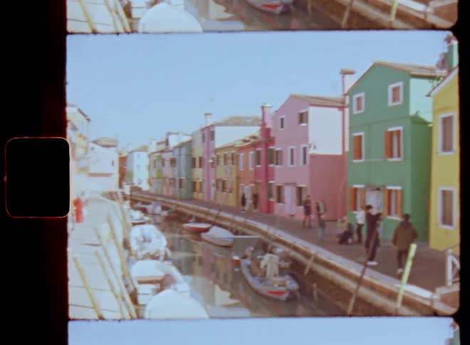 People enjoying the sunny day in the city as they are walking along a pier at a small canal with parked motor and rowing boats and colorful buildings next to each other