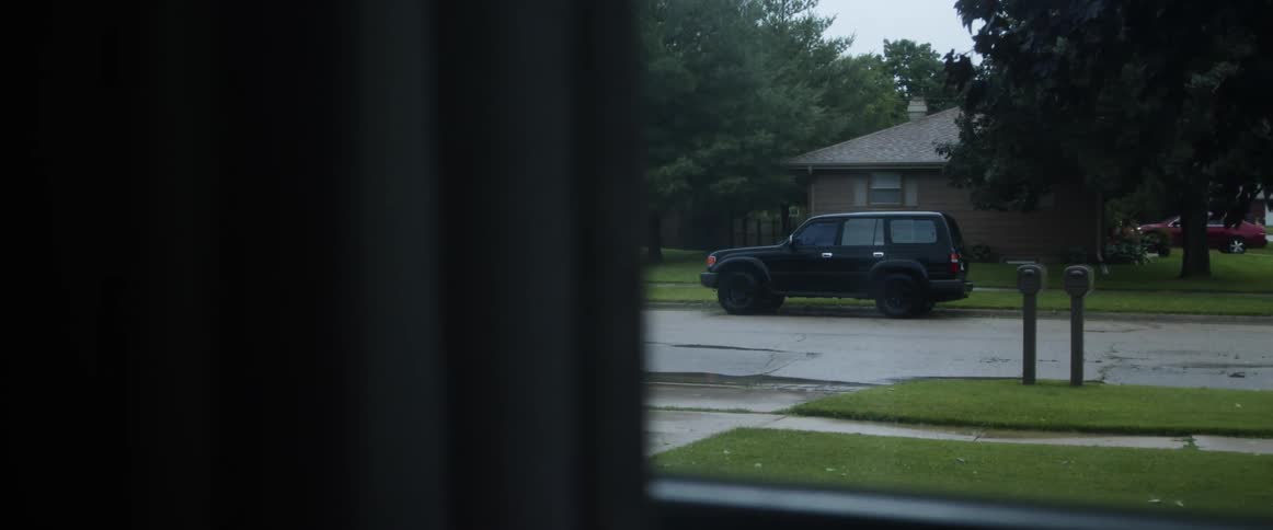 Rain falls onto residential neighborhood with cars parked both in driveways and on the street