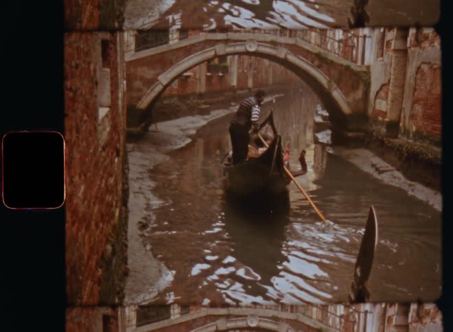 Film footage of a man rowing or paddling a gondola boat or a canoe with a long paddle or oar down a river or canal in low water driving under a small bridge surrounded by old brick or stone walls with paint peeling off