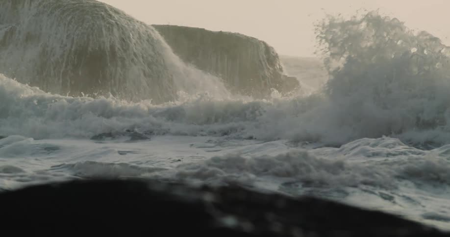 Waves flow over rocks near coast spraying water into air and foaming