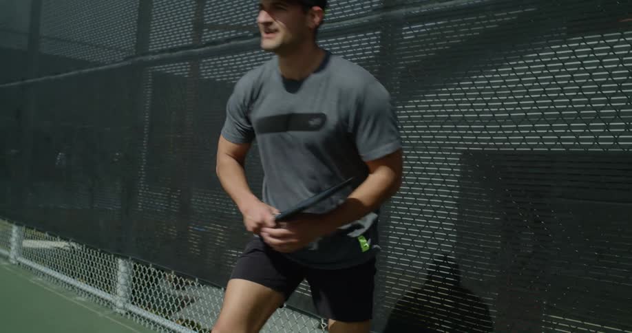Young strong man playing tennis on a court at daytime