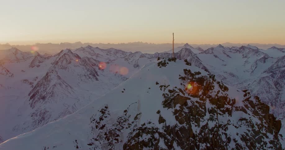 A cross sits atop snow capped mountains