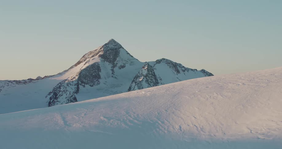 A distant peak looms over the rest of a snowy mountain range
