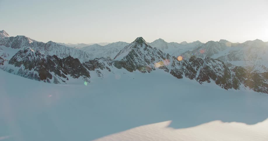 Moving over snow covered mountains as the sun shines brightly and mountains are on the horizon