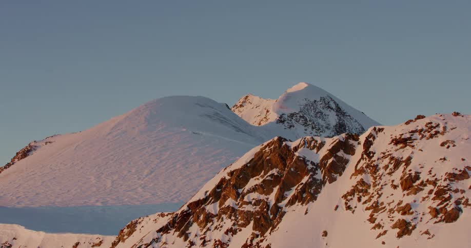 Several tall and rocky mountains are covered in a dense layer of snow