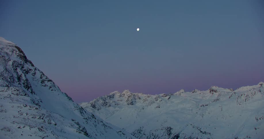 The moon is visible over the mountains at sunset