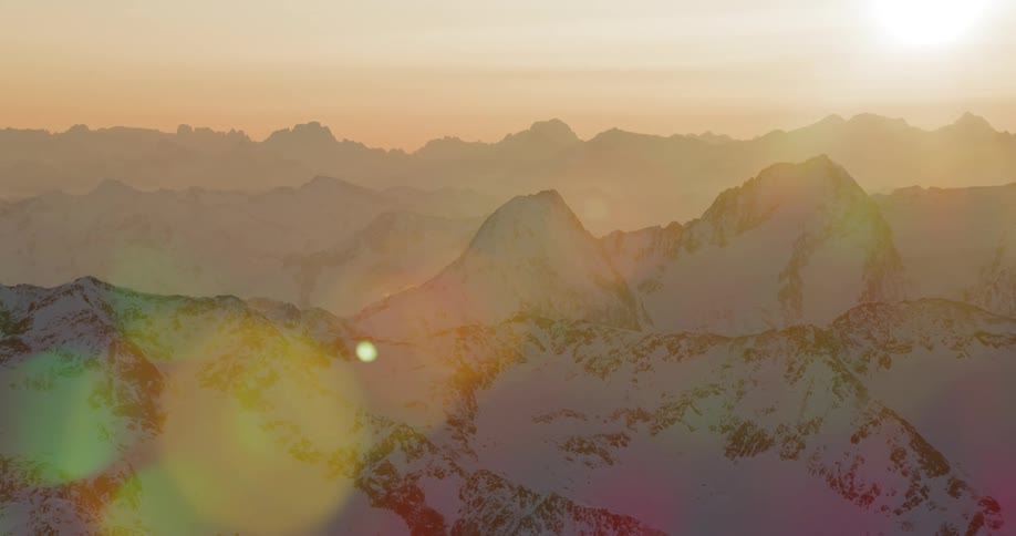 The sun shines brightly above a sprawling snow covered mountain range