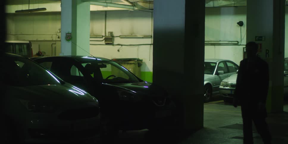 A man is walking stiffly through a parking garage