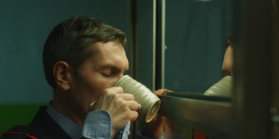 A man looks in a mirror while drinking coffee