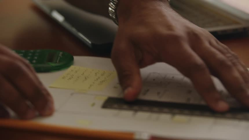 A man uses a calculator and then writes a note while reviewing a floor plan