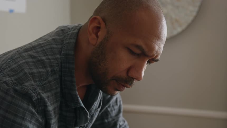 Man leans forward working before looking up and away thinking