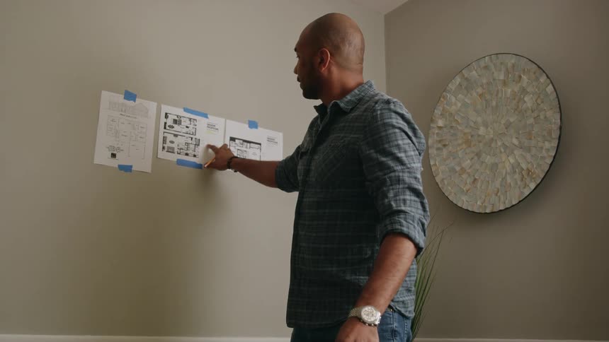 Man adds numbers while standing and working with floor plans