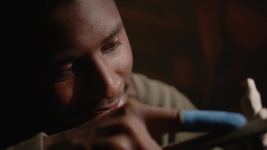 A man is looking closely as he sands a piece of wood with a file