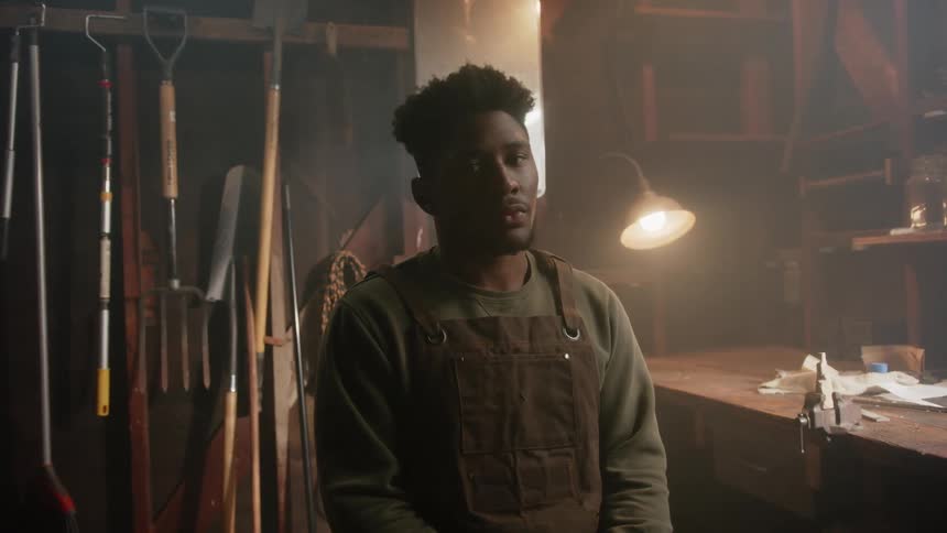 A man sitting on a stool next to a work bench looking contemplatively