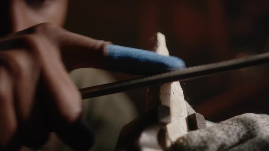 Man shapes wood in vise with a file while wearing gloves and finger covers
