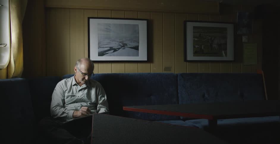 An older man sits on a couch writing or drawing