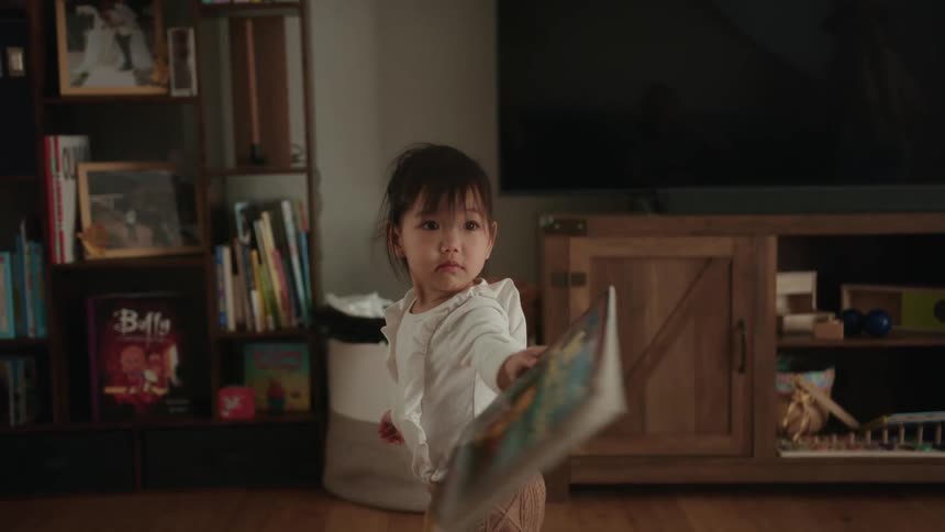 Girl with white shirt and brown pants holds book in the living room at home