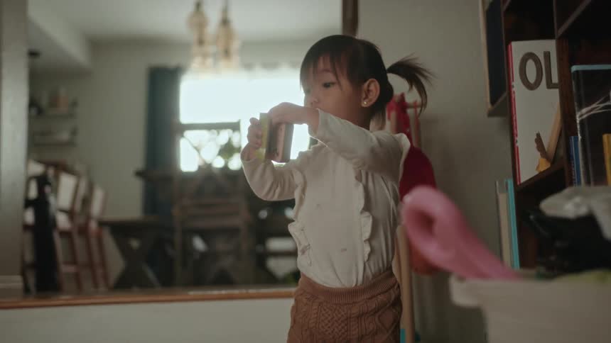 A toddler girl pulling a book off the shelf and making a shocked expression and smiling