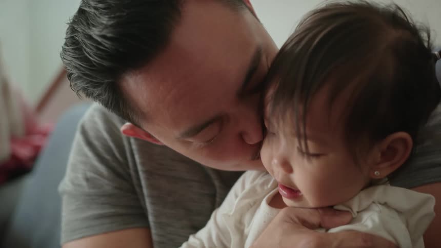 A close up of a toddler girl and her father as he kisses her on the cheek