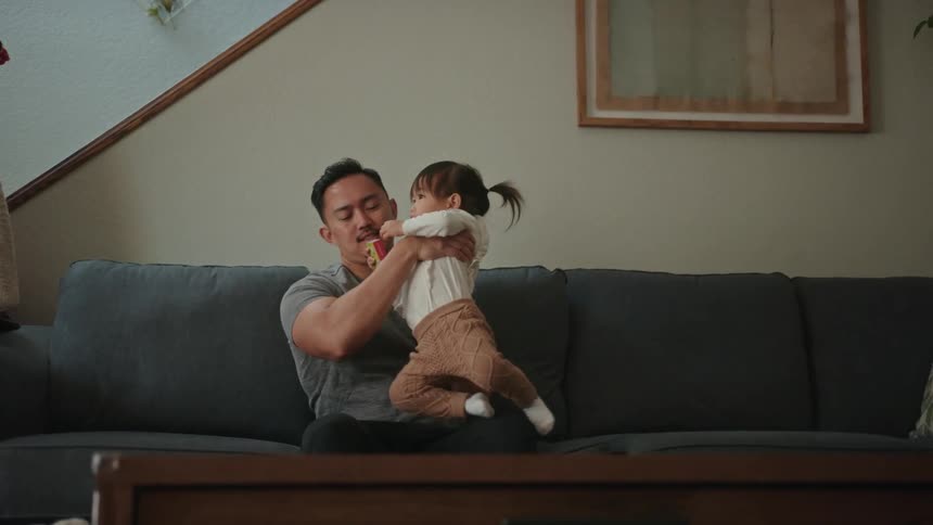 A father picking up his daughter and putting her on his lap on the couch