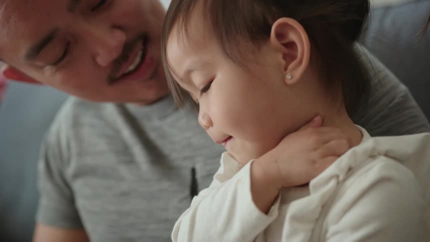 A close up of a toddler girl sitting on her fathers lap as they look down at smile