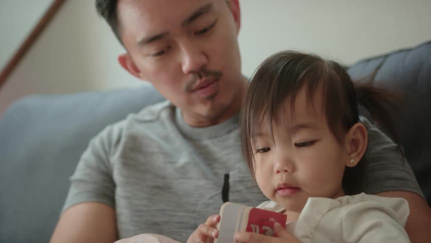 A little girl is sitting in her fathers lap as he shows her a book