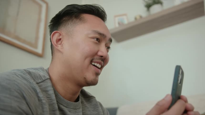 A young man is smiling and is looking at his phone