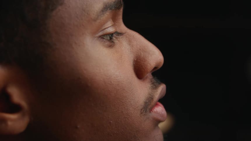 A close up of a mans face as he blows on a small piece of wood in his hands